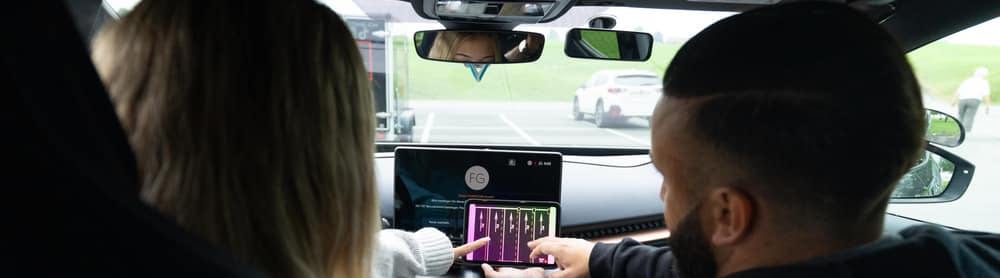 Zwei Personen sitzen in einem FAHRZONE-Fahrzeug und schauen auf den Bildschirm der Mittelkonsole.