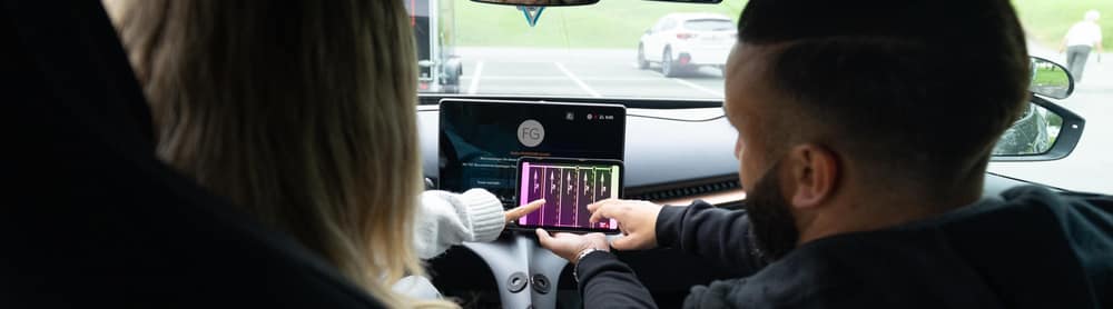 Zwei Personen sitzen in einem FAHRZONE-Fahrzeug und schauen auf den Bildschirm der Mittelkonsole.