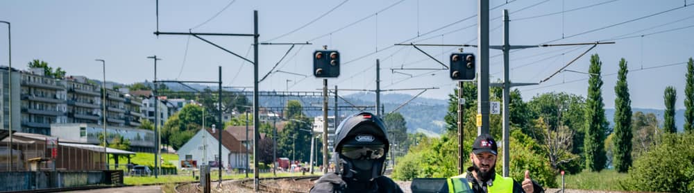 Motorradfahrer auf einem schwarzen Motorrad mit Seitenkoffern fährt an orangefarbenen Pylonen vorbei.