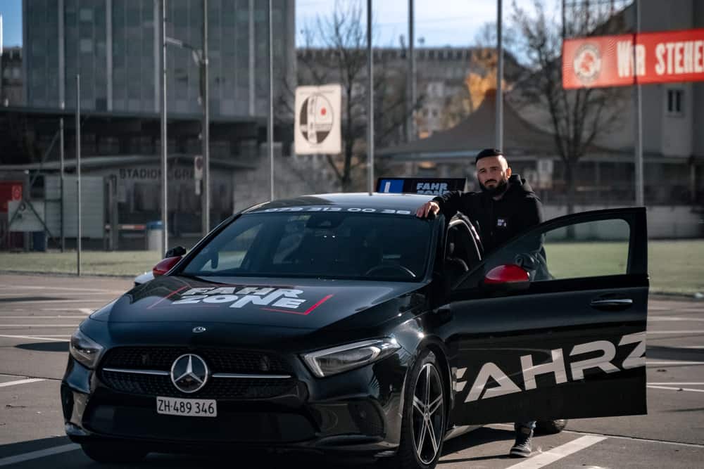 Schwarzes FAHRZONE-Fahrzeug mit geöffneter Fahrertür und einer Person daneben auf einem Parkplatz.