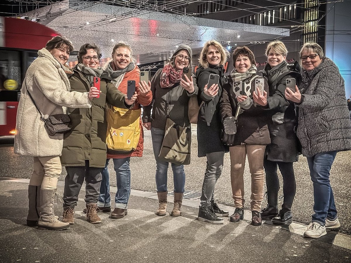 iPhone Kamera-Einstellungen erklärt: Alex Lörtscher zeigt einer Gruppe am Abend etwas am Smartphone