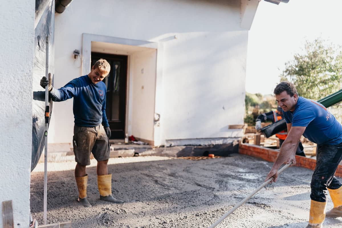Zwei Mitarbeiter verteilen frischen Beton für einen Anbau vor einem Wohnhaus