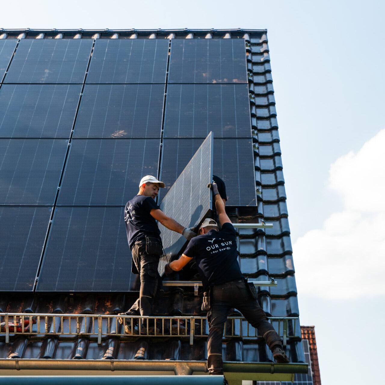 Zwei Monteure von OurSun Solar tragen ein Solarmodul auf das Dach