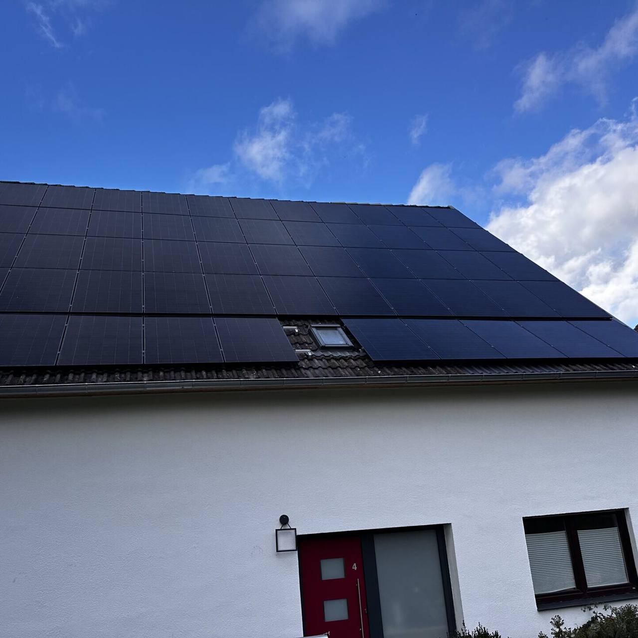 Weißes Haus mit schwarzen Solarmodulen unter blauem Himmel