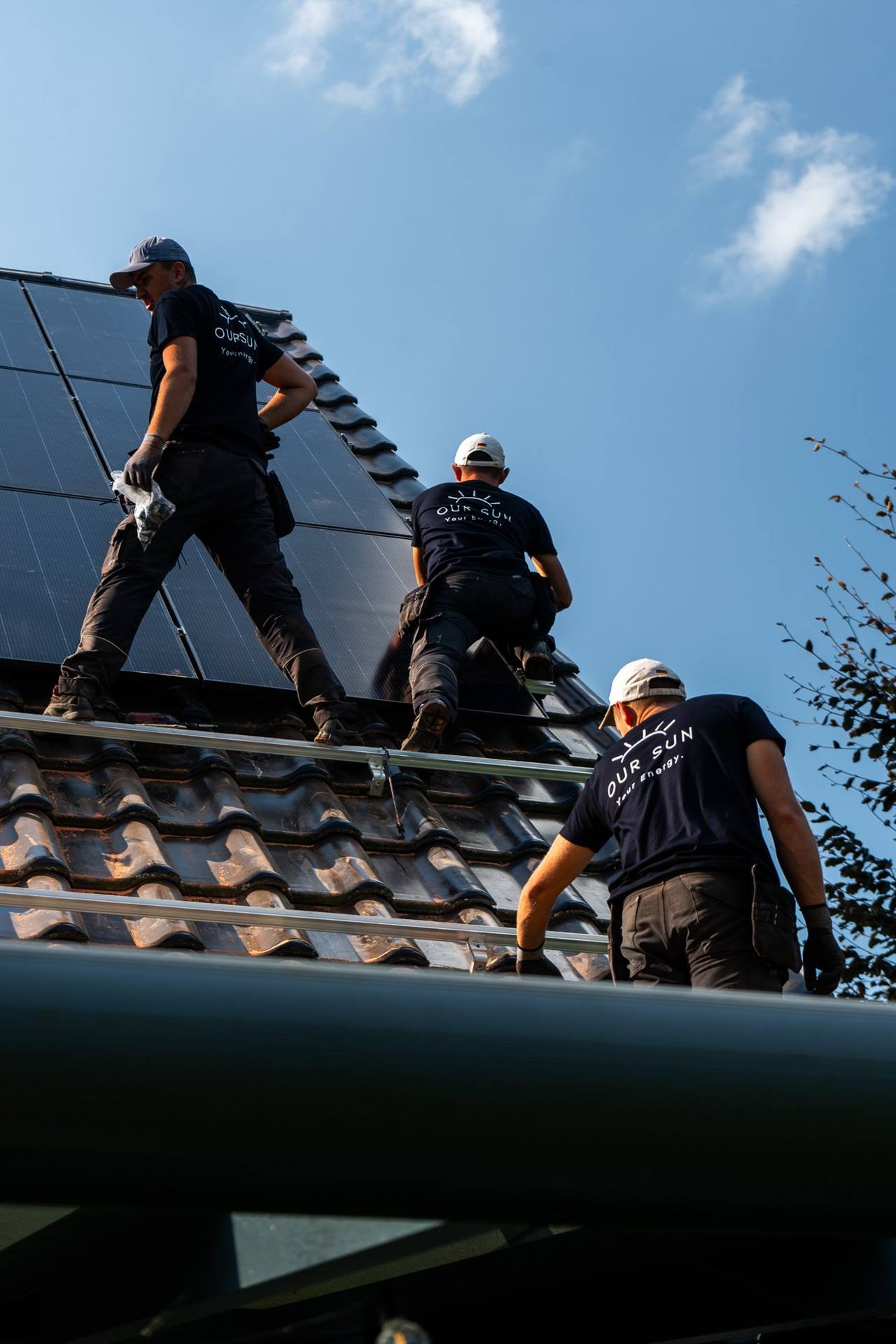 Drei OurSun-Monteure reichen ein Solarmodul auf dem Dach weiter