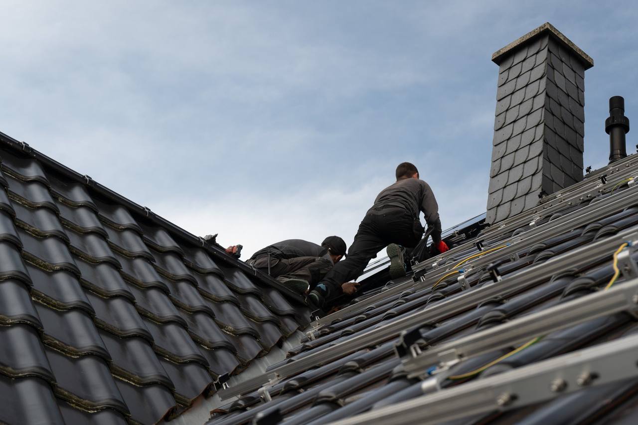 Monteure montieren Solarmodule auf einem grauen Ziegeldach neben dem Schornstein