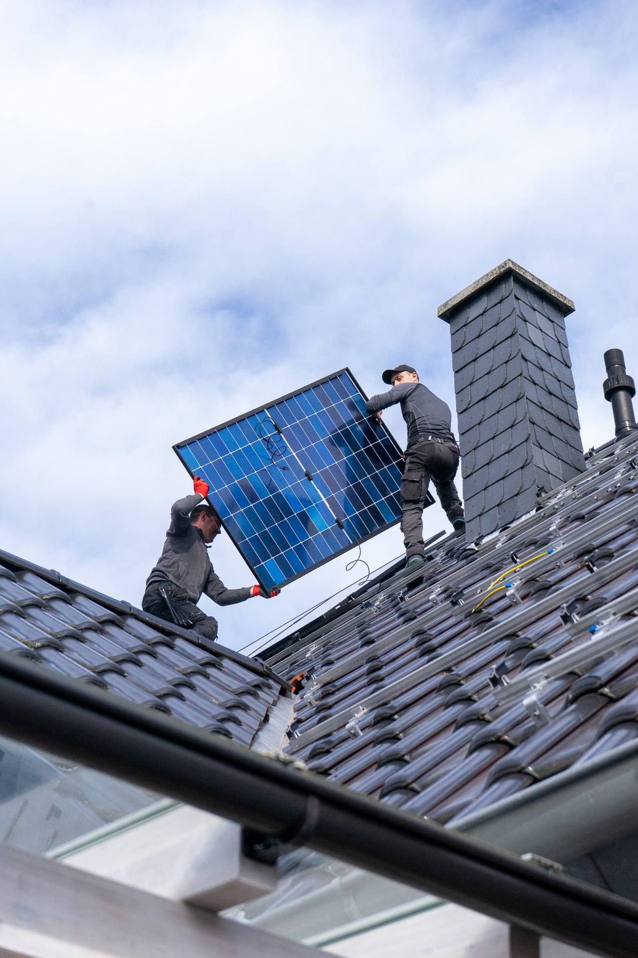 Monteure reichen ein Solarmodul über die Dachkante