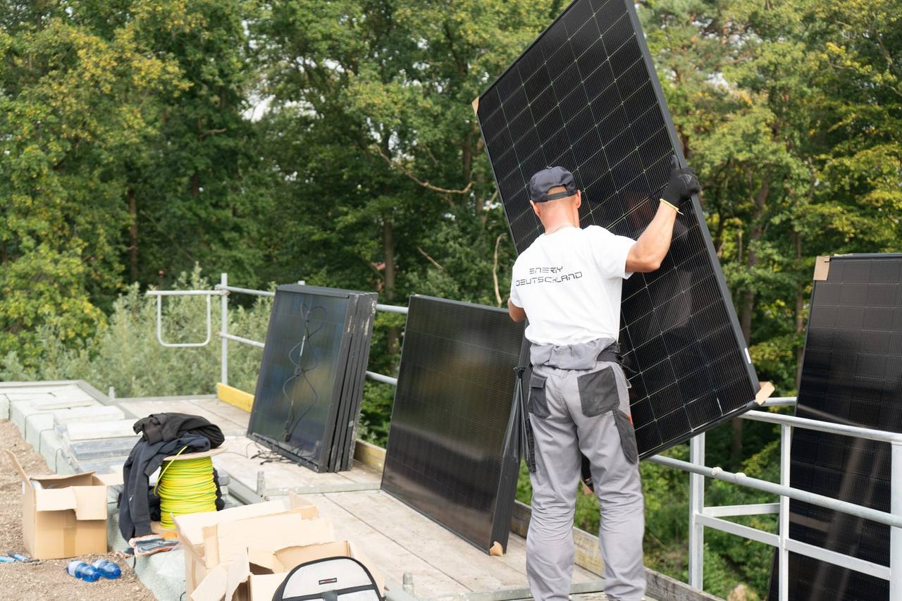 Monteur trägt ein Solarmodul über ein Flachdach