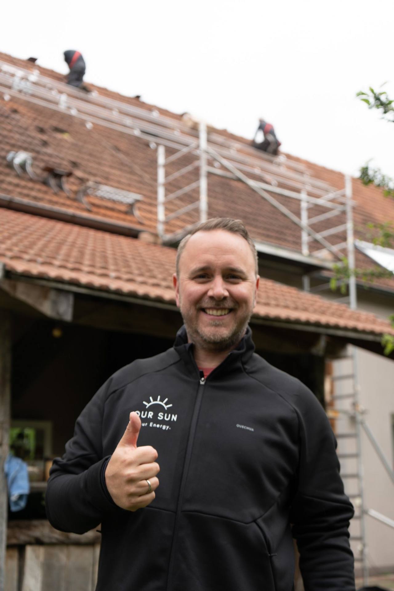 OurSun-Mitarbeiter mit Daumen hoch vor einer Baustelle