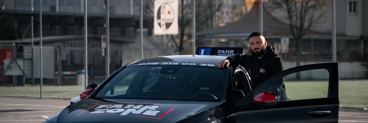 Schwarzes FAHRZONE-Fahrzeug mit geöffneter Fahrertür und einer Person daneben auf einem Parkplatz.