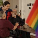 Eine Gruppe mit Regenbogenfahne, eine Person sitzt im Rollstuhl