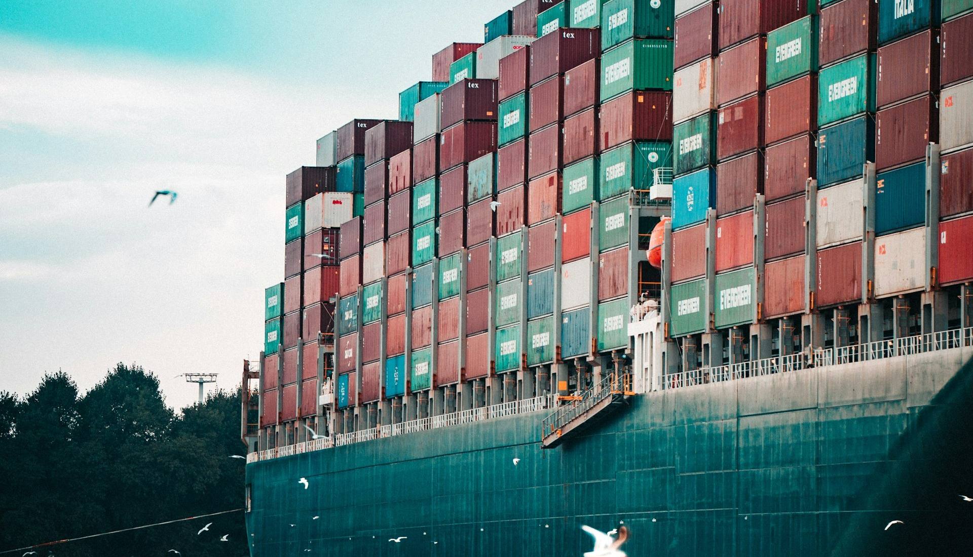 Großes Containerschiff mit bunten Frachtcontainern auf dem Wasser, Möwen fliegen umher.