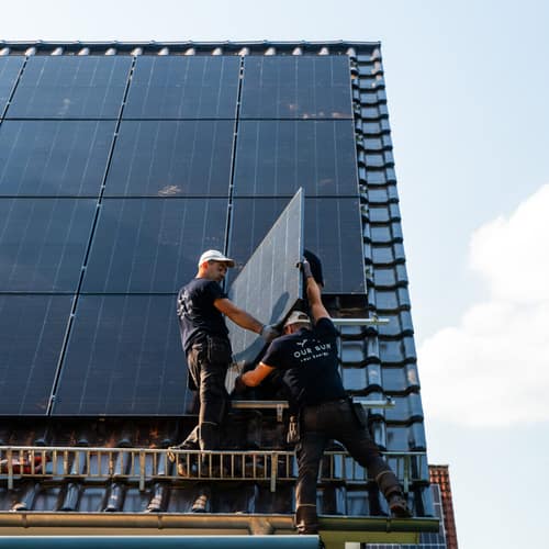 Zwei Monteure tragen ein Solarmodul über das Gerüst aufs Dach