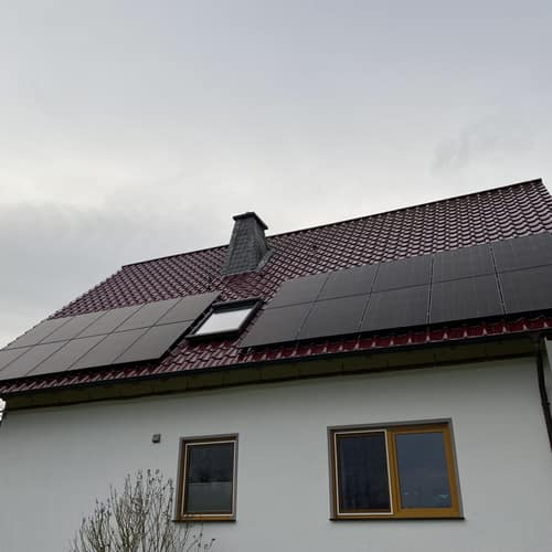 Weißes Haus mit rotem Ziegeldach und Solarmodulen