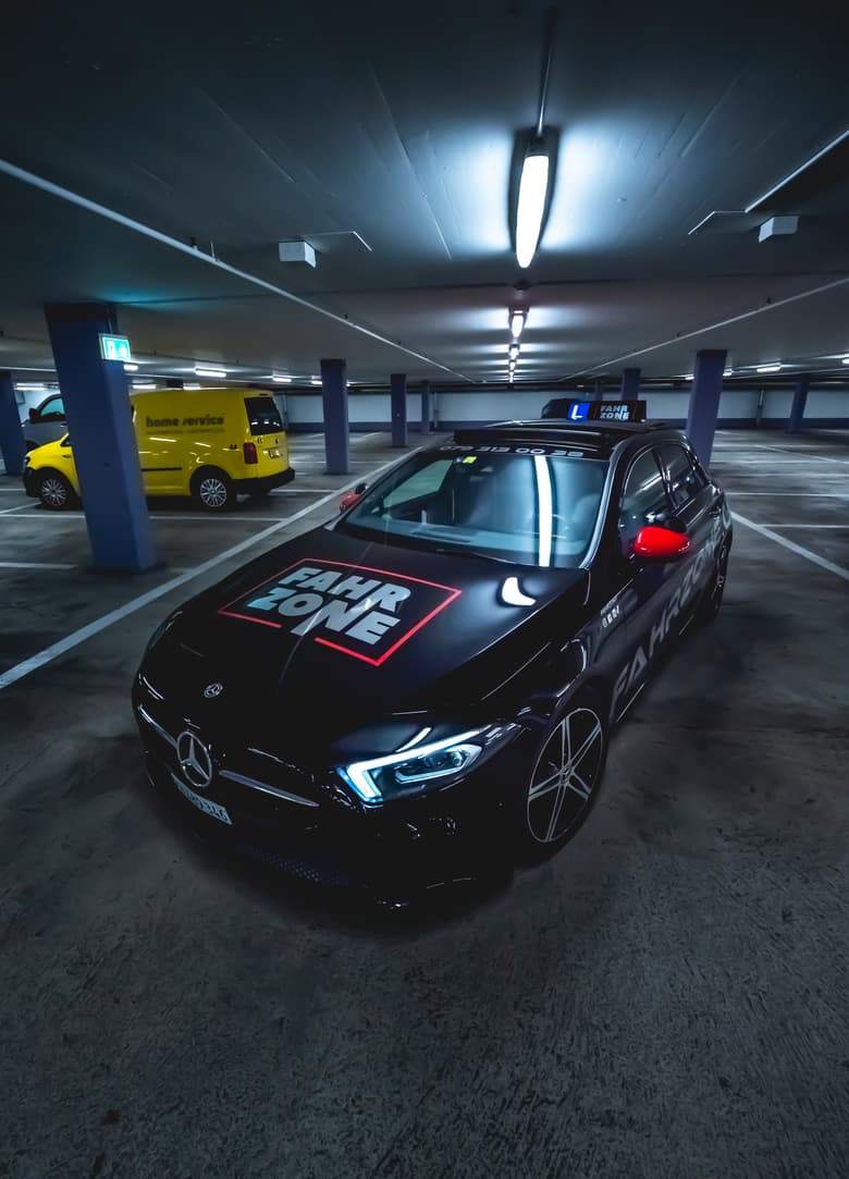 Motorhaube eines roten Autos mit FAHR-ZONE-Schriftzug in einer Tiefgarage.