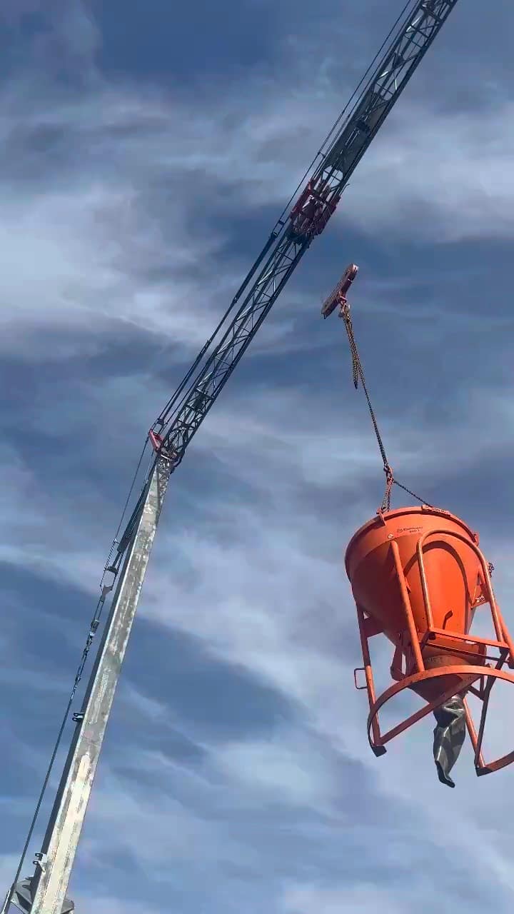 Krankübel mit Beton hängt am Baukran vor blauem Himmel