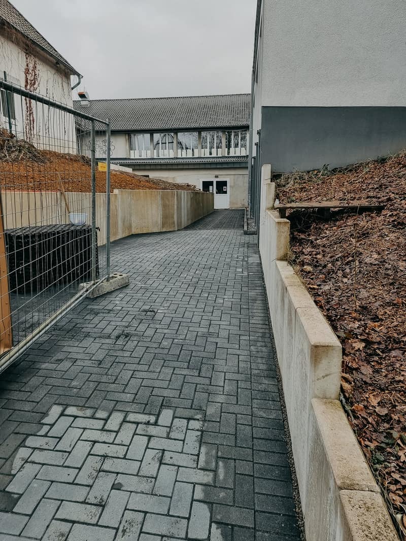 Gepflasterter Weg entlang einer Stützwand aus Winkelsteinen am Hang