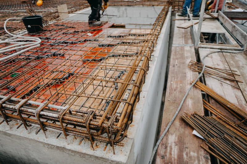 Bewehrung für eine Betondecke auf roter Schalung, dahinter Mitarbeiter