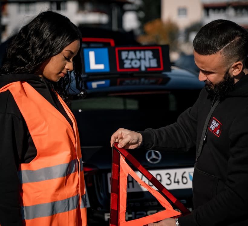 Fahrlehrer mit Fahrschülerin und Warndreieck beim Sichern.