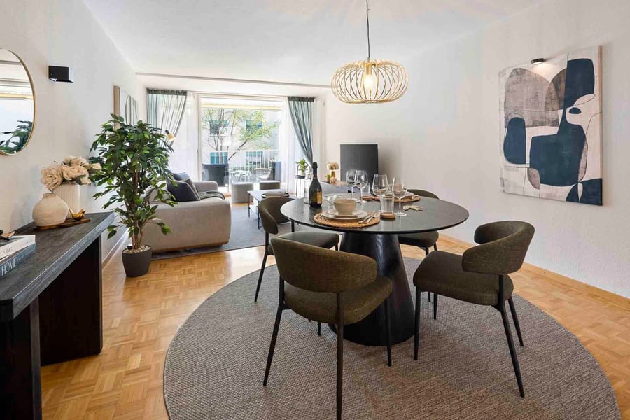 Wohnzimmer der Wohnung von Daheim auf Zeit in St. Gallen: runder Esstisch, dunkle Polsterstühle, Parkett und Blick auf den hellen Balkon