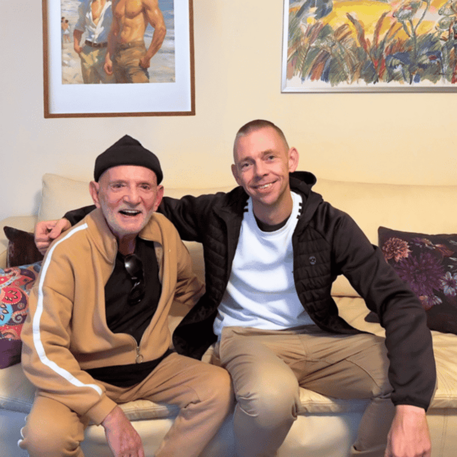 Zwei lächelnde Männer sitzen nebeneinander auf einem Sofa.