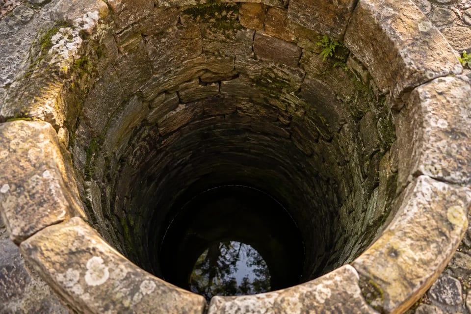 Blick in einen tiefen, aus Naturstein gemauerten Brunnen mit Wasser am Grund