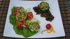 Drei grüne Frikadellen auf Salatblättern mit Paprikawürfeln, dazu Spinat, getrocknete Tomaten und eine Kirschtomate.