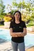 Lächelnde Frau namens Julia im schwarzen Garten-und-Landschaftsbau T-Shirt vor einem Pool und grünem Garten.
