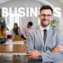 Ein lächelnder Geschäftsmann in Anzug und Brille mit verschränkten Armen vor dem Text "BUSINESS" und einem Büro.