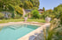 Moderner Swimmingpool mit Steintreppe in einem grünen Garten mit Rasenfläche, großen Pflanzkübeln und Gartenhaus im Hintergrund.