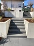 Moderne Gartenanlage mit dunklen Steinstufen zwischen hellen L-Steinen aus Beton und Beeten mit Rindenmulch.