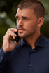 Mann in navyblauem Hemd telefoniert konzentriert – stilvoller Business-Look für den Alltag.

