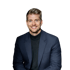 Ein lächelnder junger Mann mit blonden Haaren, blauem Anzug und schwarzem Rollkragenpullover.