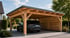 Ein dunkles Auto parkt in einem modernen Doppelcarport aus hellem Holz mit Flachdach und seitlicher Sichtschutzwand.