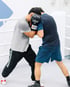 Zwei Männer trainieren Nahkampf in einem Boxring, einer trägt schwarze Fairtex-Boxhandschuhe.