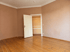 Leeres Zimmer mit Holzdielenboden, beigefarbenen Wänden und einer offenstehenden weißen Zimmertür.