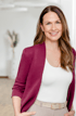 Saskia Pihaly mit schulterlangen braunen Haaren, einem weinroten Blazer, weißem Top und beiger Hose.