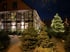 Fachwerkhaus mit beleuchteten Fenstern und Weihnachtsbaum mit Lichterketten im dunklen Wintergarten.