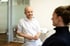 Ein lächelnder Zahnarzt in weißem Kittel spricht mit einer Patientin.