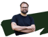 Ein lächelnder Mann (Malte) mit Brille, Bart und Tätowierung am Oberarm 