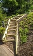 Eine Holztreppe führt einen mit Rindenmulch bedeckten Hang mit grünen Pflanzen hinauf