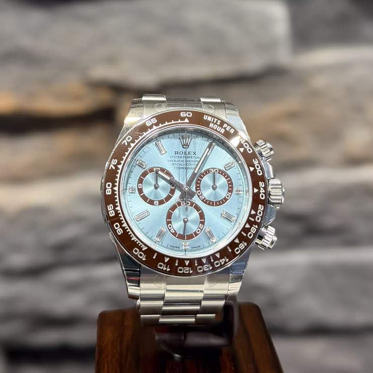 Eine silberne Rolex Daytona mit hellblauem Zifferblatt und brauner Lünette auf einem Holzständer.