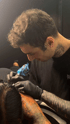 Cristian, ein Tätowierer des Walk in Tattoo-Studios in Backnang, konzentriert bei der Arbeit an einem Tattoo, mit schwarzen Handschuhen und Tätowiermaschine in der Hand.