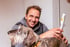 Ein lächelnder Mann hält ein weißes medizinisches Lasergerät an den Rücken eines drahthaarigen Hundes.