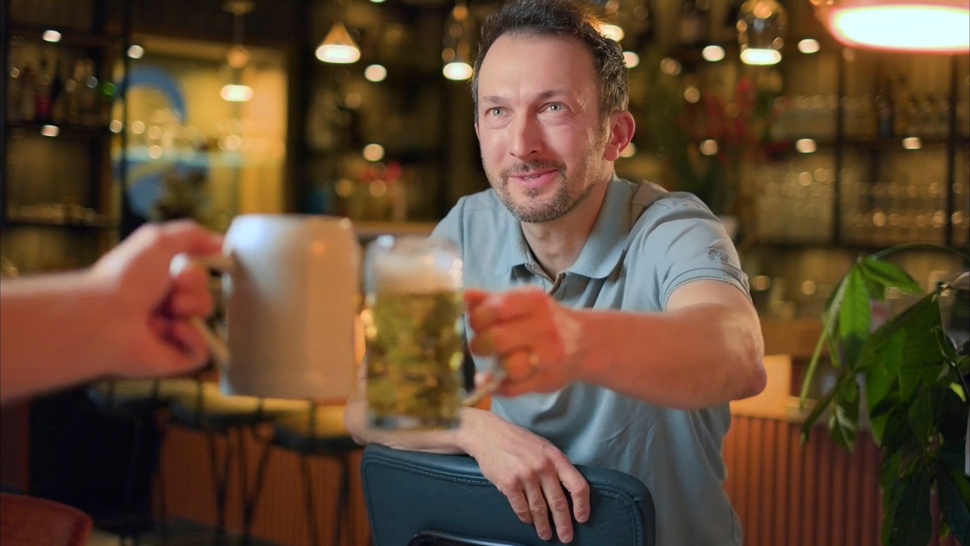 Gastgeber im aatal.HAUS stößt an der Bar mit einem Bierkrug an