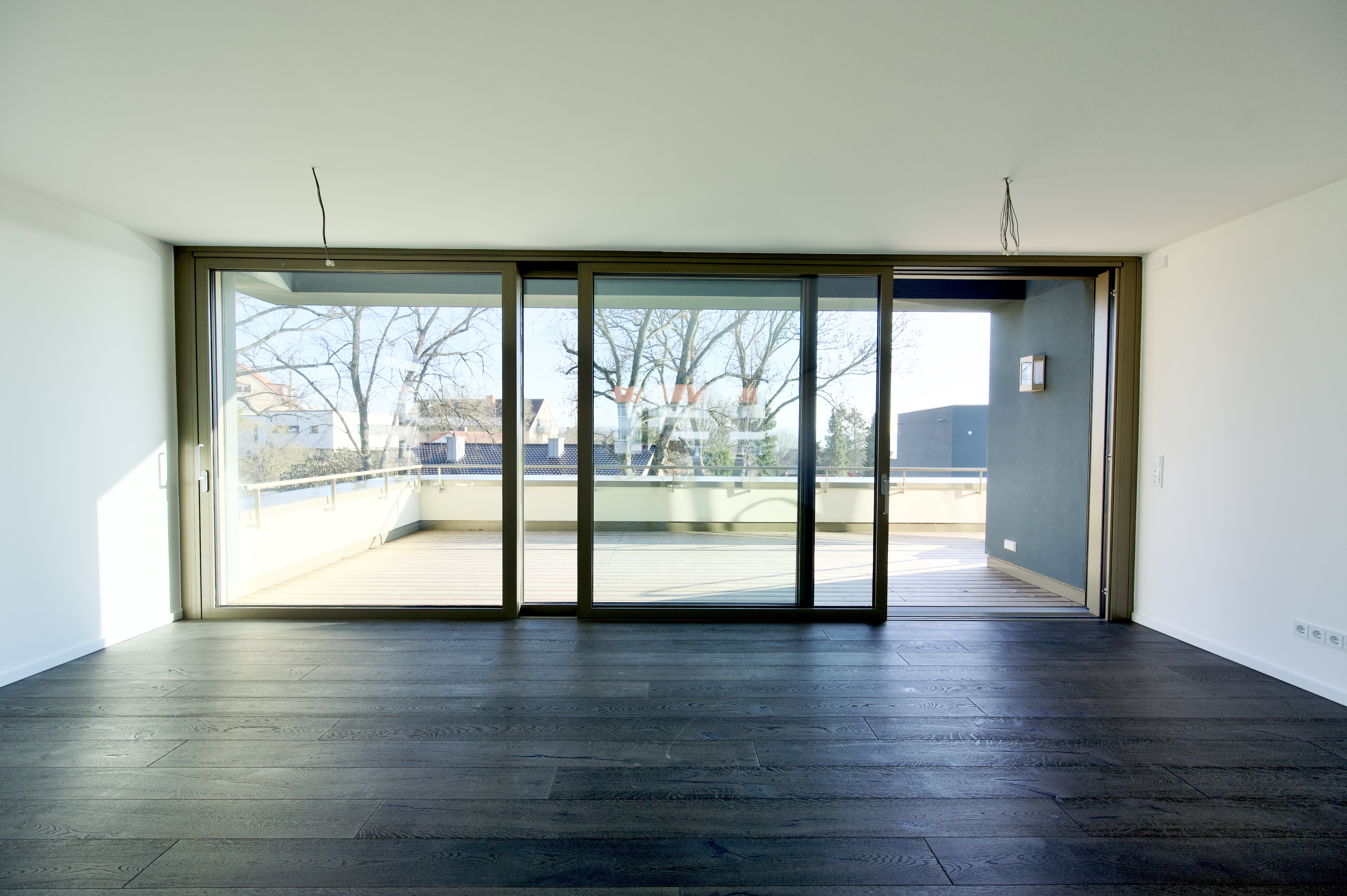 Projekt Himmelsruh – Wohnraum mit dunklem Holzboden und großer Glasfront zur Terrasse