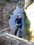 Mann in Neoprenanzug und Helm seilt sich von Felswand über grünem Wasser ab.