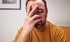 Ein Mann mit Bart und gelbem Rollkragenpullover hält die Hand vor sein Gesicht.