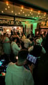 Ein DJ legt Musik auf, während Gäste auf einer Party unter Lichterketten und grüner Beleuchtung tanzen.