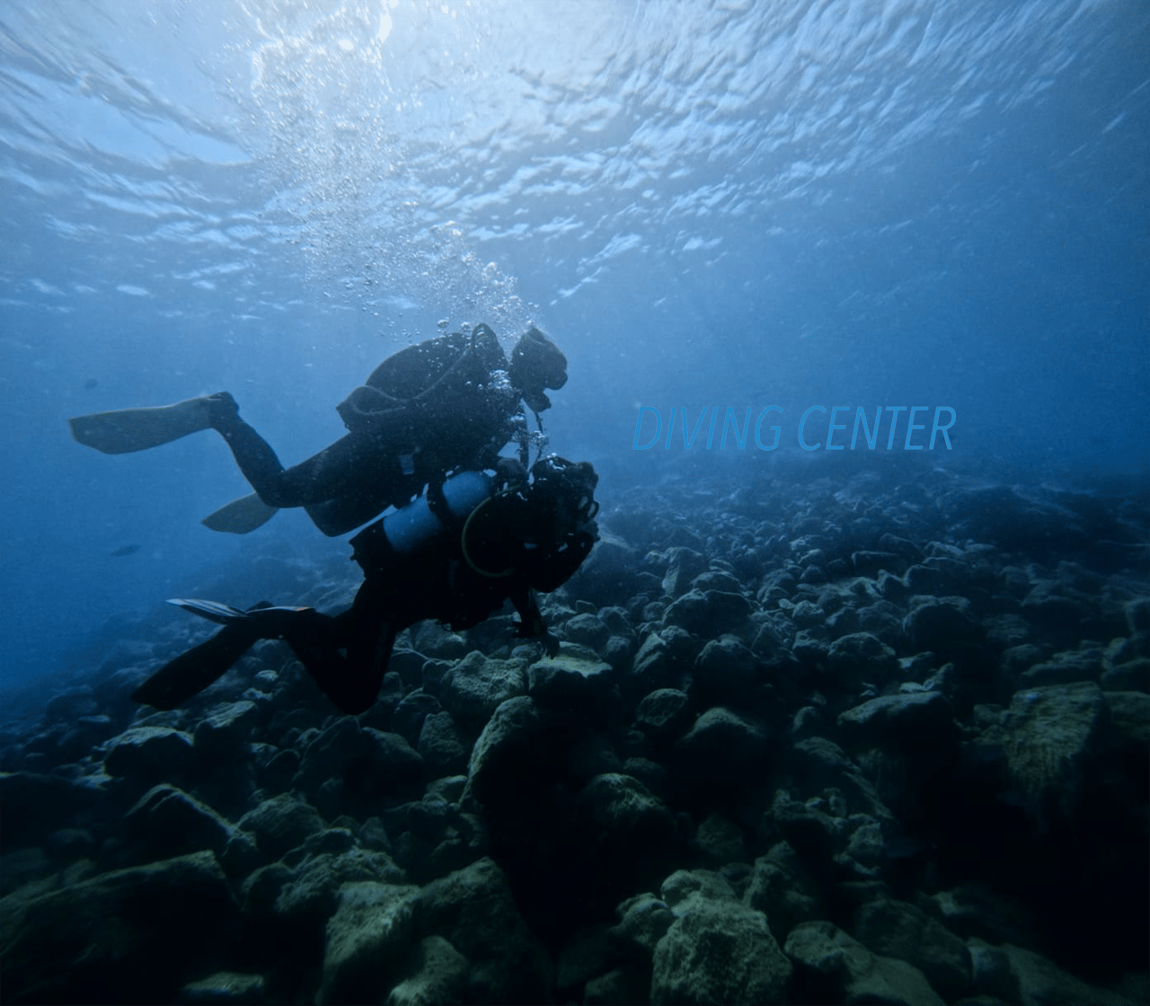 Two scuba divers gliding over a rocky reef in clear blue water